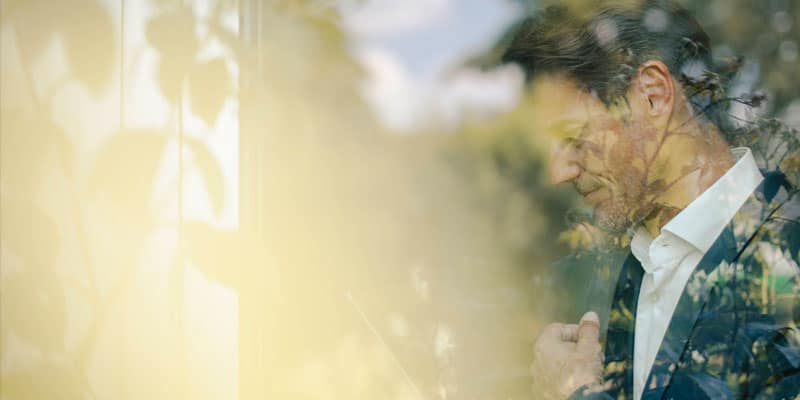 Gott im Alltag - Ein junger Mann in nachdenklicher Pose ist kaum zu erkennen, weil eine Scheibe Licht reflektiert