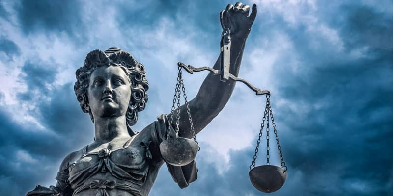 Gott im Alltag - Justitia mit der Waage als Hüterin des Rechts und der Gerechtigkeit vor einem bedrohlichen Himmel